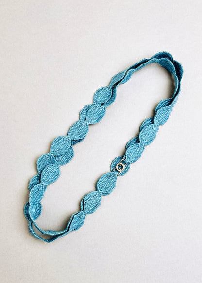 Overhead view of sky blue interwoven cotton ovals necklace placed in a double loop with sterling silver endings on a grey background