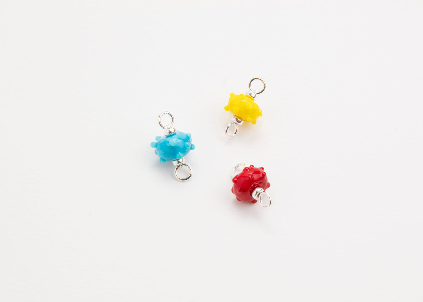 Front view of a trio of urchin lampwork glass charms with Sterling Silver ends in a white background