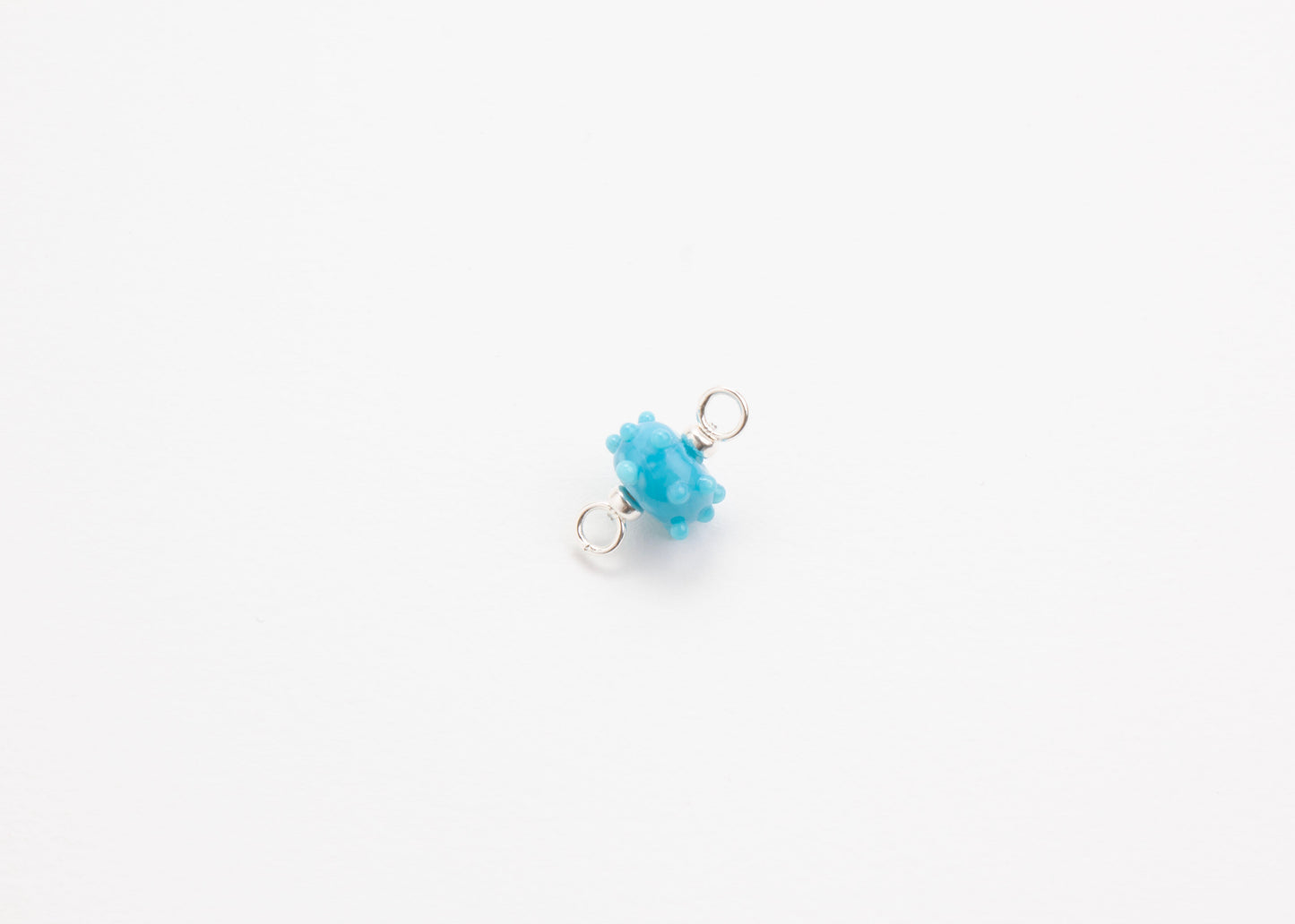 Diagonal view of an urchin lampwork glass blue charm with Sterling Silver ends in a white background