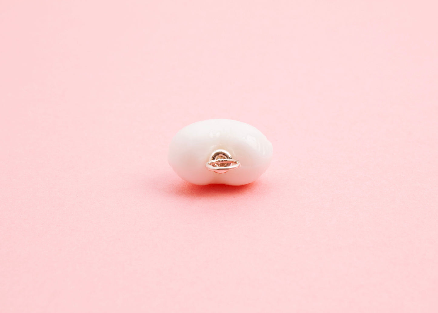 Close up of the Sterling Silver looped endings detail of white lampwork glass heart charm on a pink background