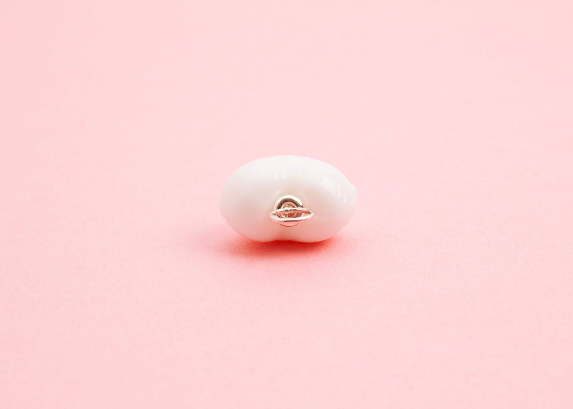 Close up of the Sterling Silver looped endings detail of white lampwork glass heart charm on a pink background