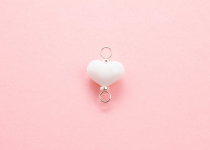 Plan view of white lampwork glass heart charm with Sterling Silver looped endings on a pink background