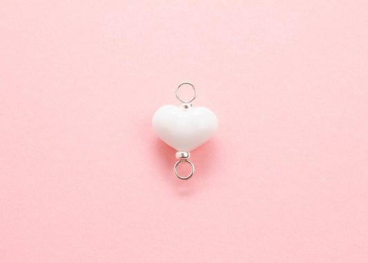 Plan view of white lampwork glass heart charm with Sterling Silver looped endings on a pink background