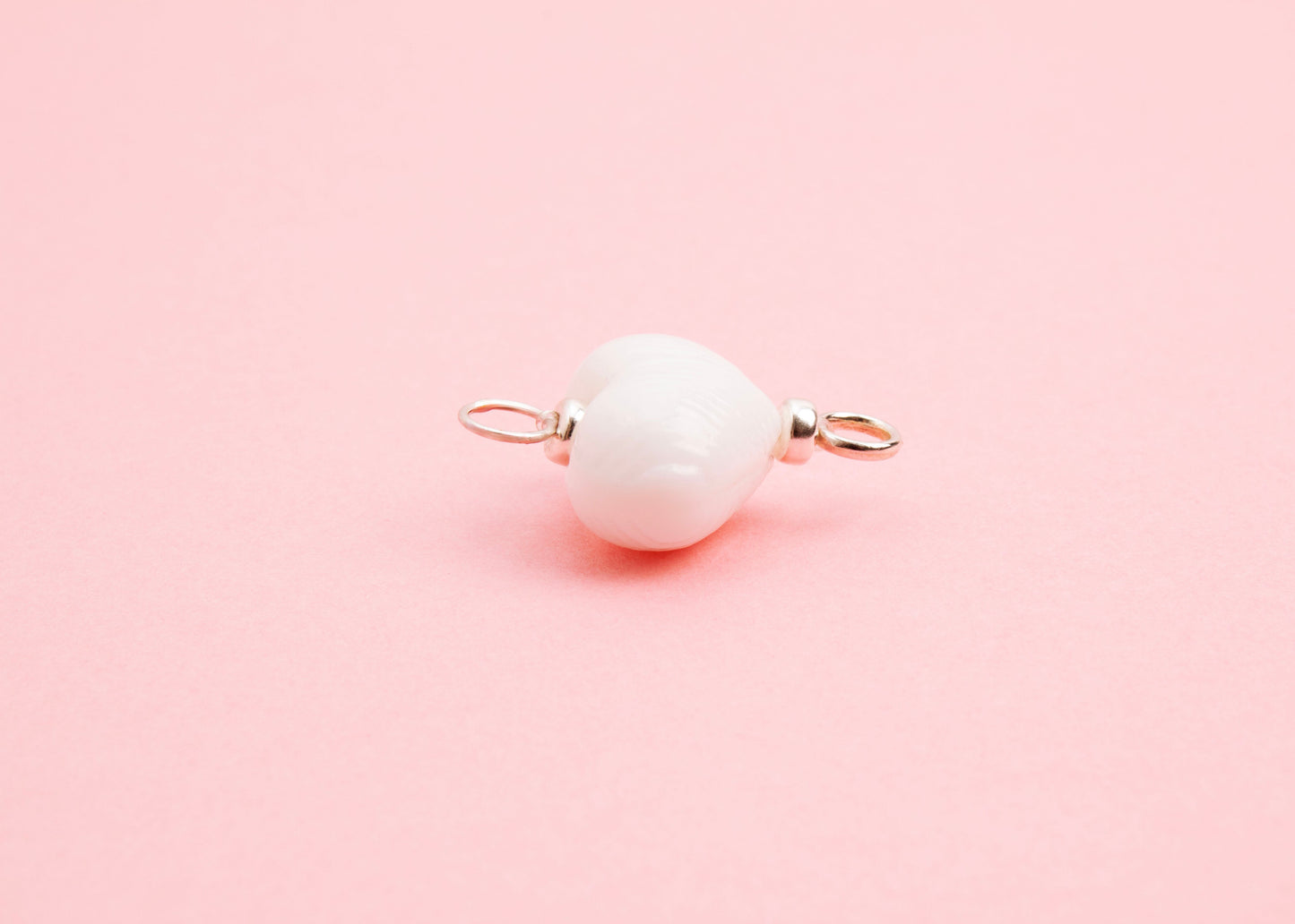Side view of white lampwork glass heart charm with Sterling Silver looped endings on a pink background