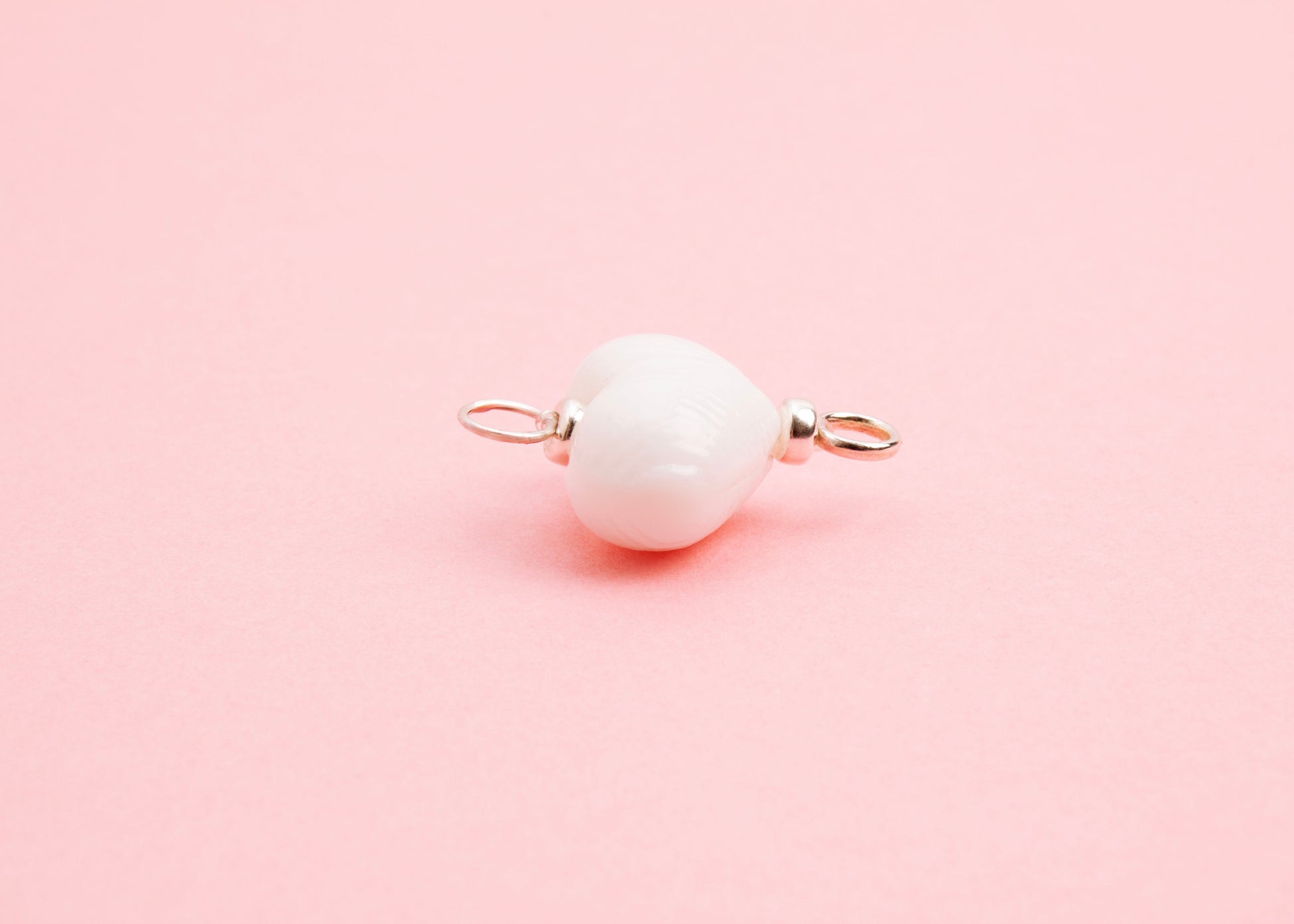 Side view of white lampwork glass heart charm with Sterling Silver looped endings on a pink background