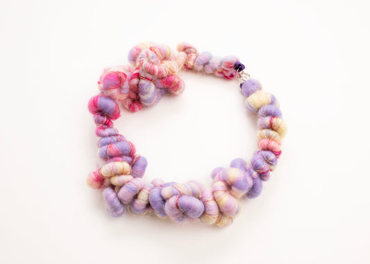 Plan view of a wool yarn closed necklace in cream, lavender, deep pink, purple and gold accents with Sterling Silver looped endings on a white background