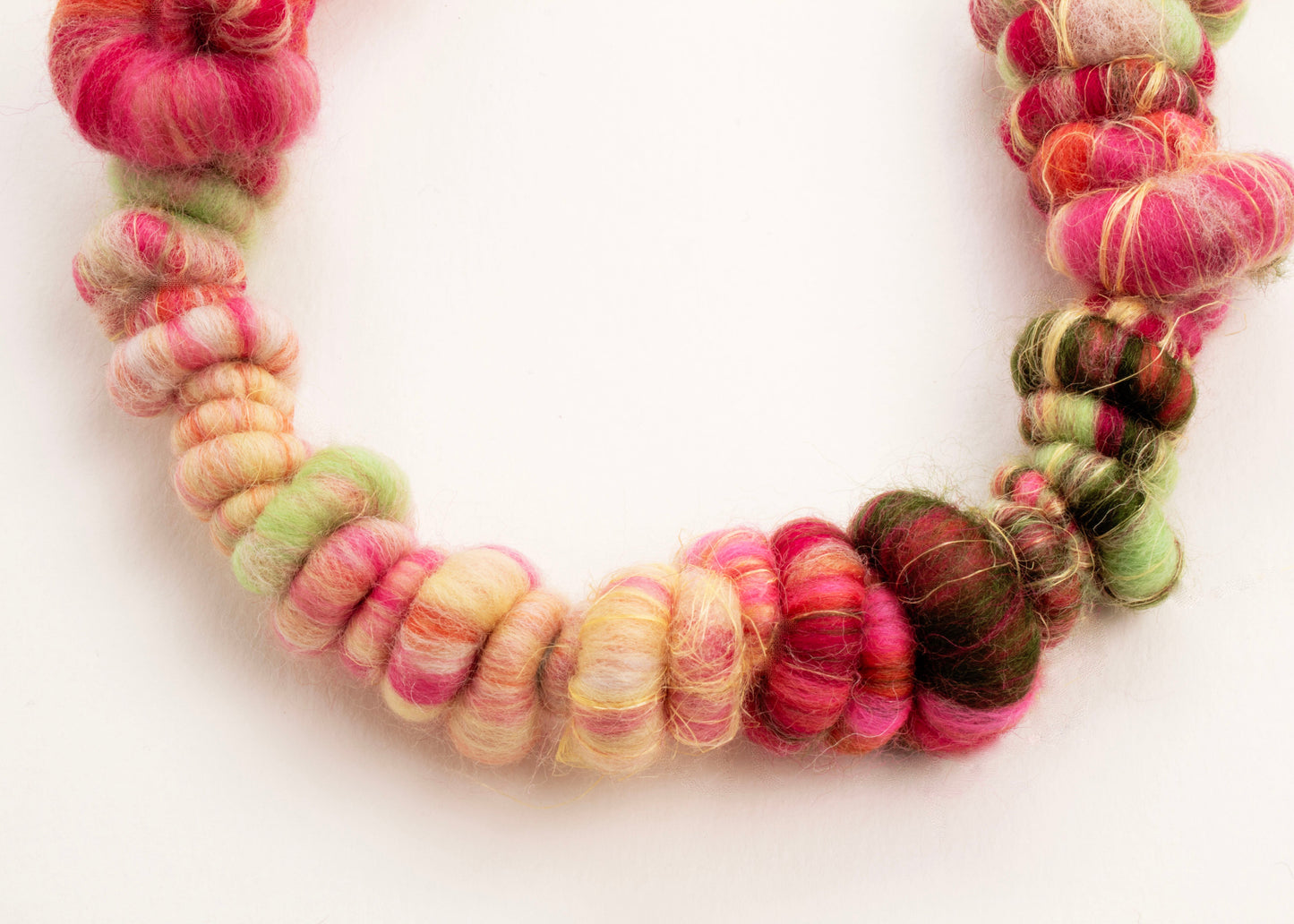 Close up of the drop detail of a wool yarn closed necklace in persimmon, peach, butter yellow, mint and forest green  with Sterling Silver looped endings on a white background