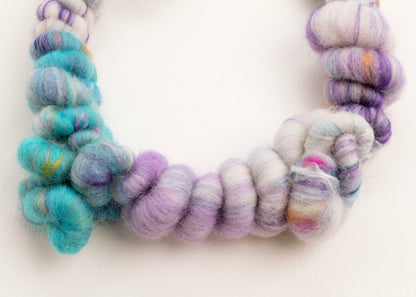 Close up drop detail  of a wool yarn necklace in cream, turquoise, purple and hazelnut accents with Sterling Silver looped endings on a white background
