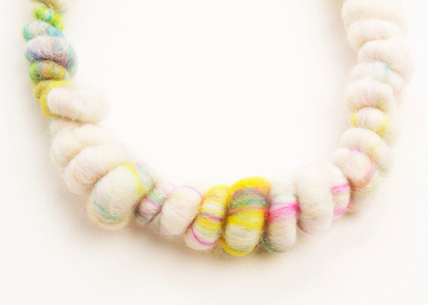 Close up drop detail of a wool yarn necklace in ivory, with bright colours accents with Sterling Silver looped endings on a white background