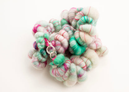 Plan view of a wool yarn necklace twisted in a knot in cream, teal, and deep pink accents with Sterling Silver looped endings on a white background