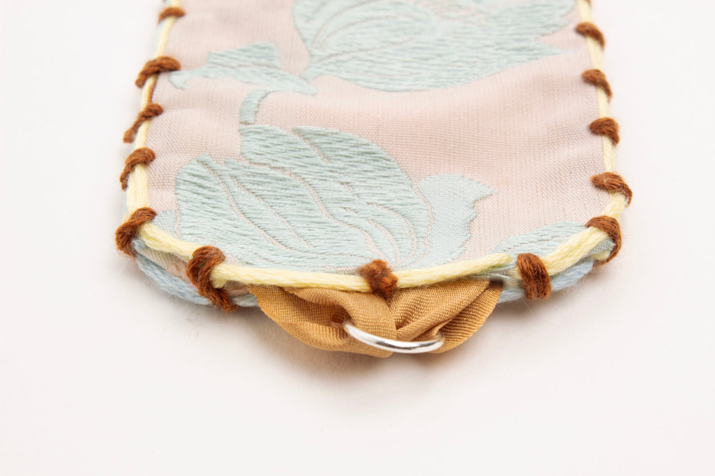 Detail of Sterling Silver looped endings with caramel brown silk ribbon of reversible cotton woven strap bracelet with tulip motif in light blue and embroidered borders in brown, light blue and butter yellow on a white background.