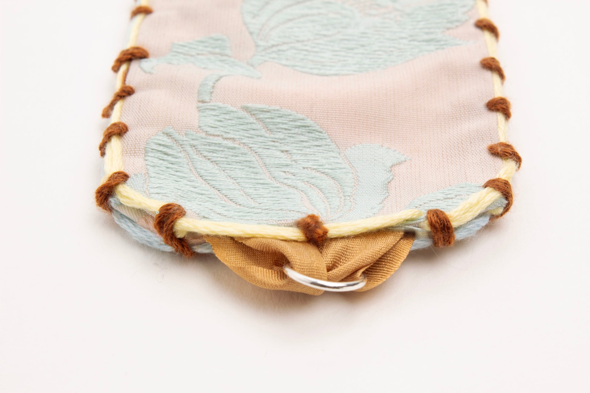 Detail of Sterling Silver looped endings with caramel brown silk ribbon of reversible cotton woven strap bracelet with tulip motif in light blue and embroidered borders in brown, light blue and butter yellow on a white background.