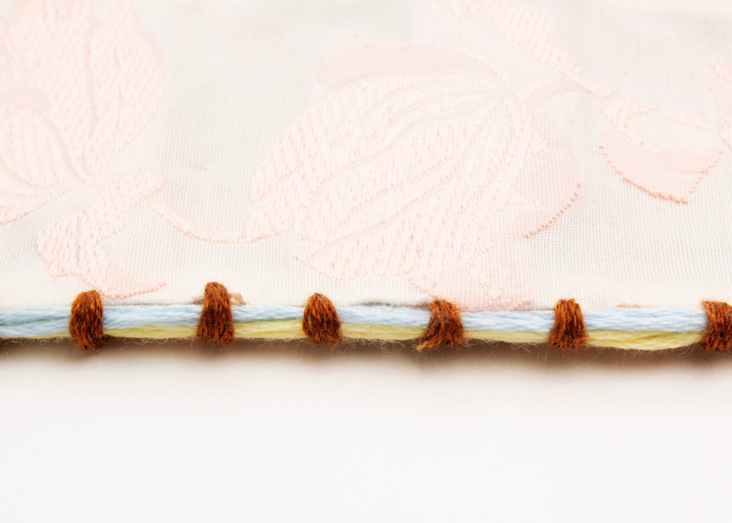 Detail of embroidered border of reversible cotton woven strap bracelet with tulip motif in pink and embroidered borders in brown, light blue and butter yellow with Sterling Silver looped endings detail on a white background.