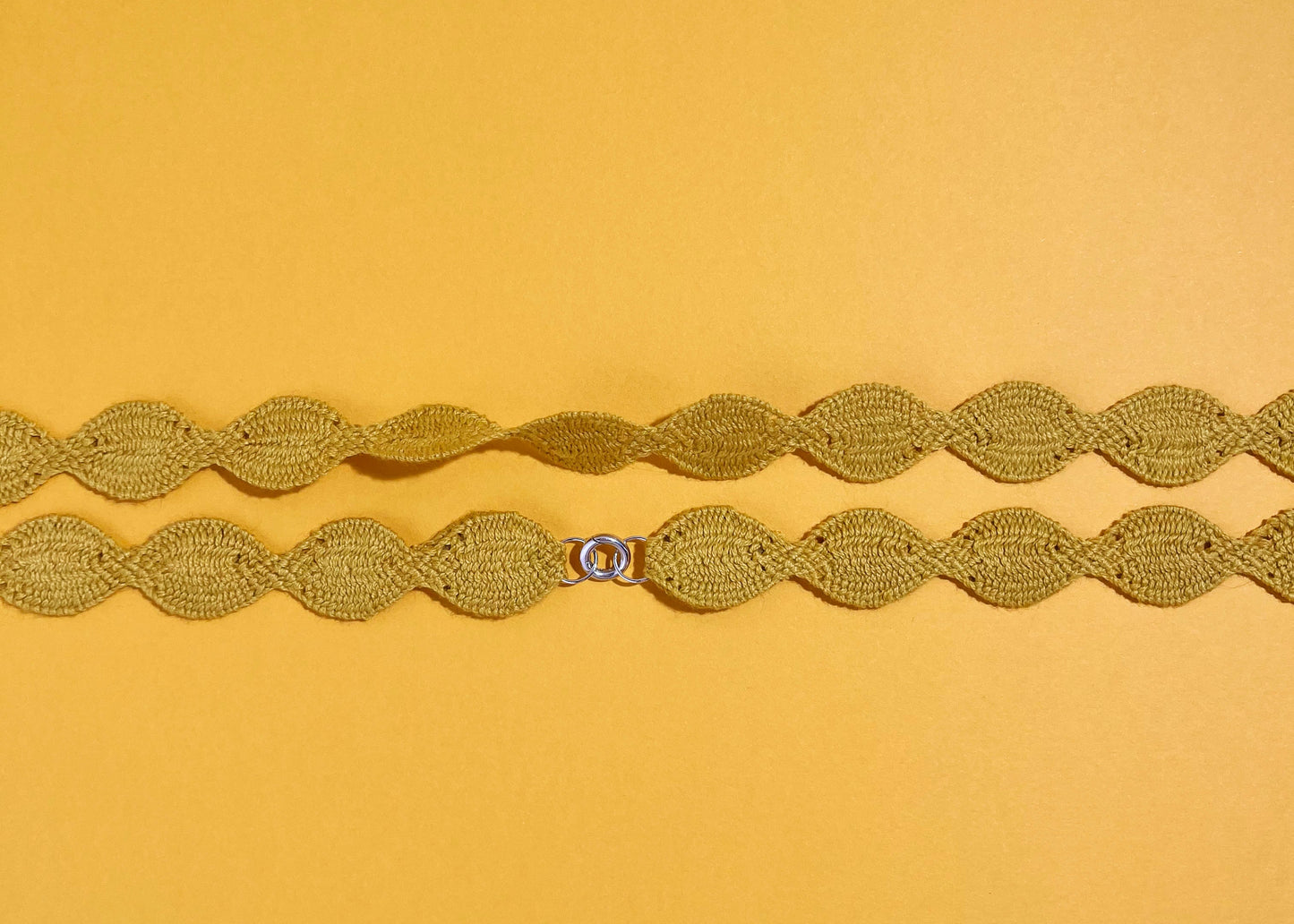 Overhead close look at the fabric and endings of a yellow cotton woven necklace placed horizontally with sterling silver endings on a yellow background