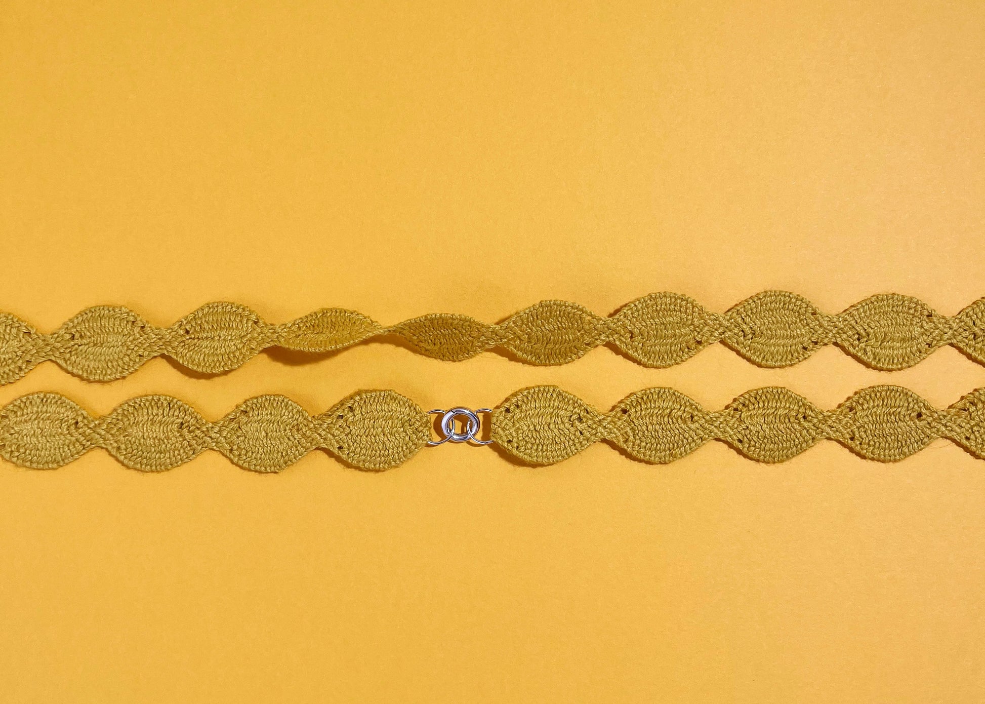 Overhead close look at the fabric and endings of a yellow cotton woven necklace placed horizontally with sterling silver endings on a yellow background