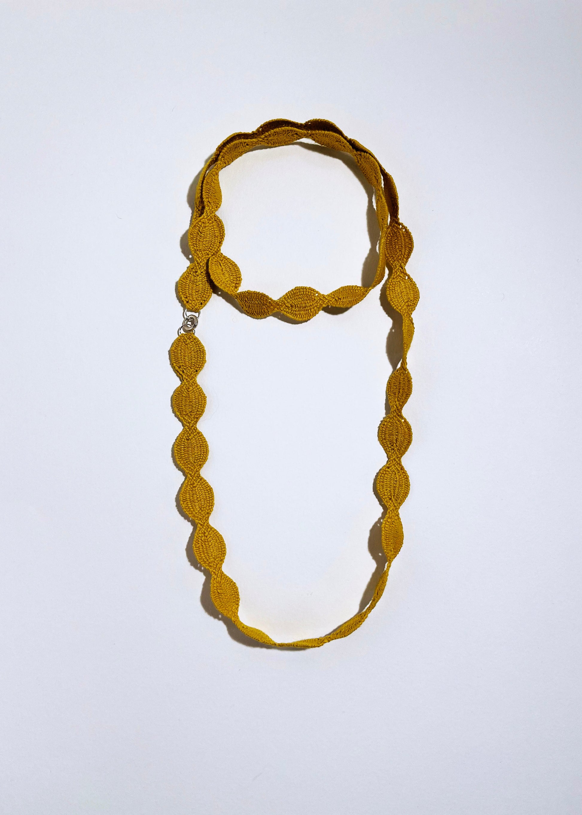 Overhead view of a yellow cotton woven necklace placed in double loop as a chocker with sterling silver endings on a white background