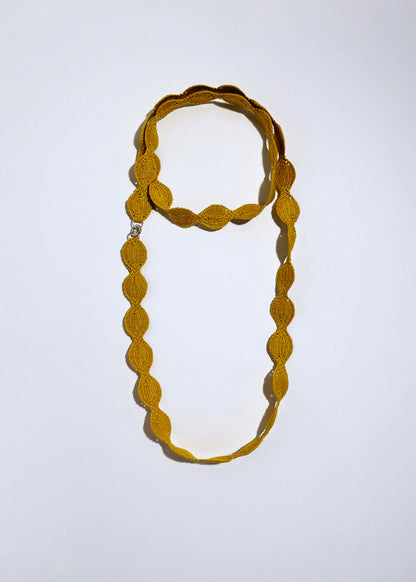 Overhead view of a yellow cotton woven necklace placed in double loop as a chocker with sterling silver endings on a white background