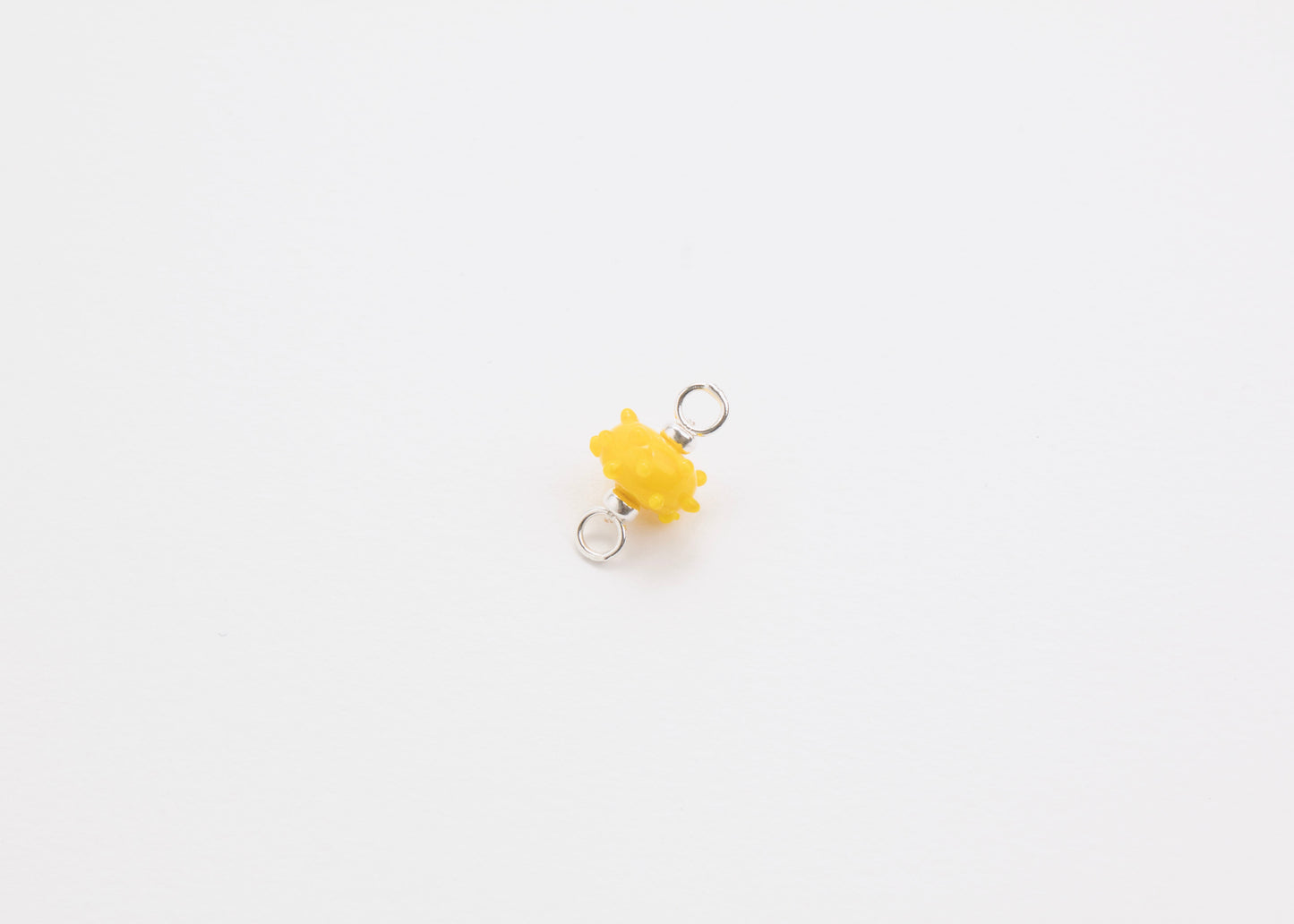 Diagonal view of a yellow urchin lampwork glass charm with Sterling Silver ends in a white background