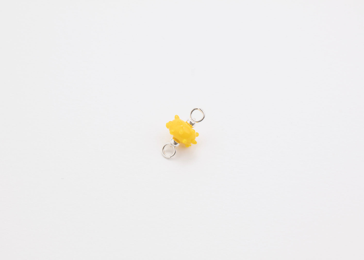 Diagonal view of a yellow urchin lampwork glass charm with Sterling Silver ends in a white background