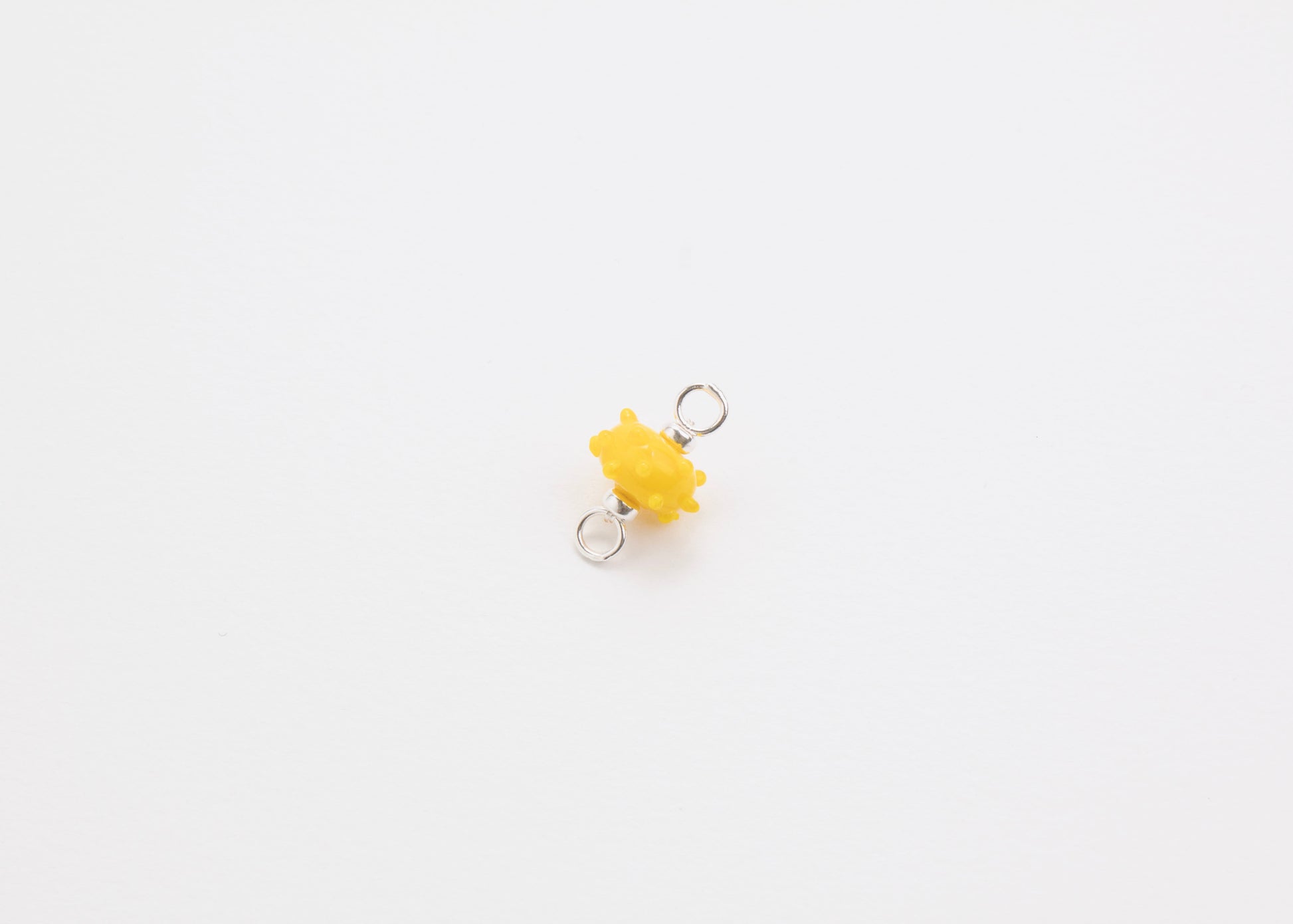 Diagonal view of a yellow urchin lampwork glass charm with Sterling Silver ends in a white background